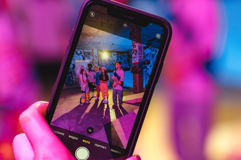 Auf einem Smartphone ist ein Foto, auf dem Jugendliche in pinkem Licht tanzen.