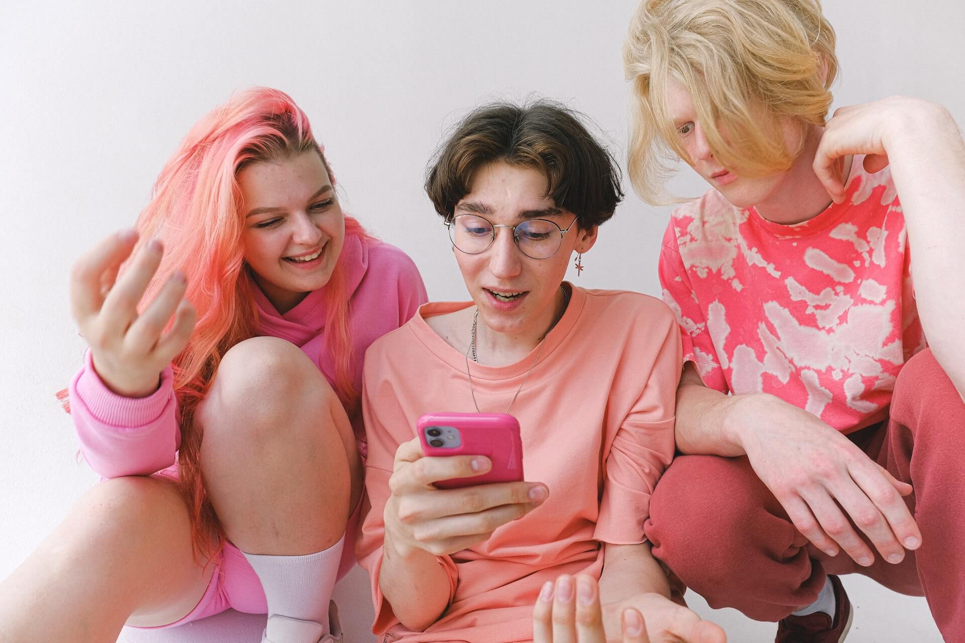 Drei Teenager in pinken Outfits schauen auf ein Handy und wundern sich.