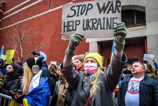 Hilfe für die Ukraine: Auf einer Friedendesmo hält eine blonde, hellhäutige Frau mit gelber Wollmütze ein Plakat hoch.