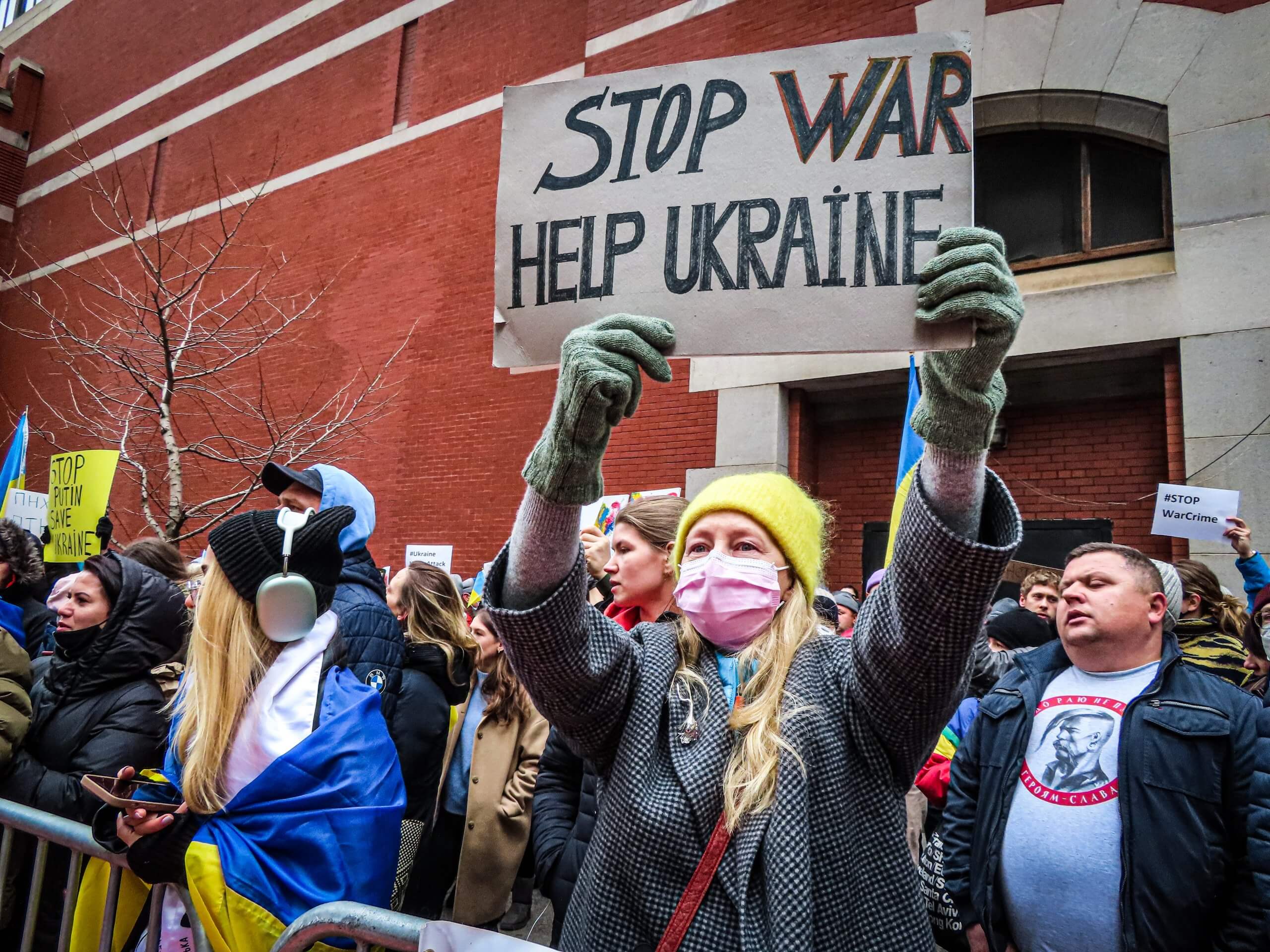 Hilfe für die Ukraine: Auf einer Friedendesmo hält eine blonde, hellhäutige Frau mit gelber Wollmütze ein Plakat hoch.