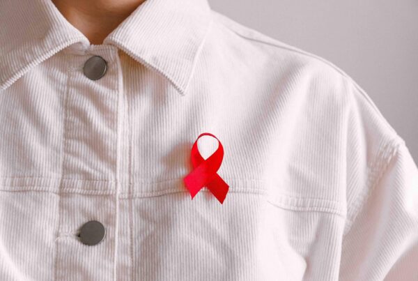 Zu sehen ist eine weiße Jacke mit roter Awareness-Schleife für den Welt-Aids-Tag